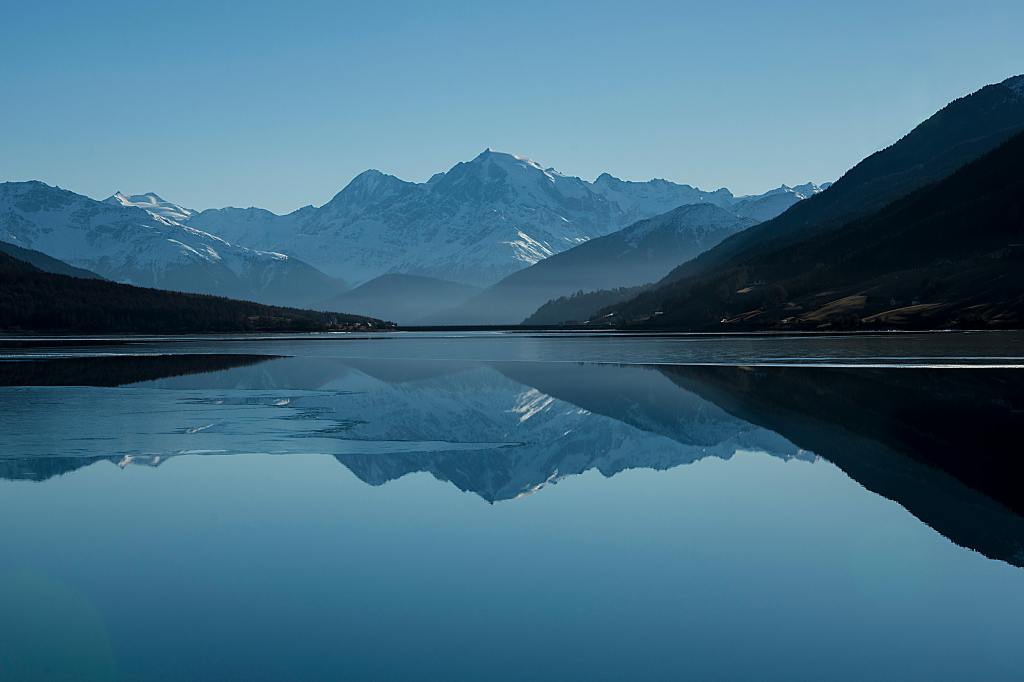 a snowy mountain reflected in an icy lake